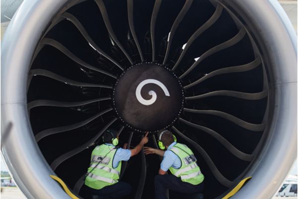 Two ground crew members dressed in high-visibility vests and headsets, are examining the inside of an aircraft engine.