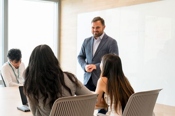 A Cathay Pacific employee wearing a suit jacket is giving a presentation to three team members in a conference room.