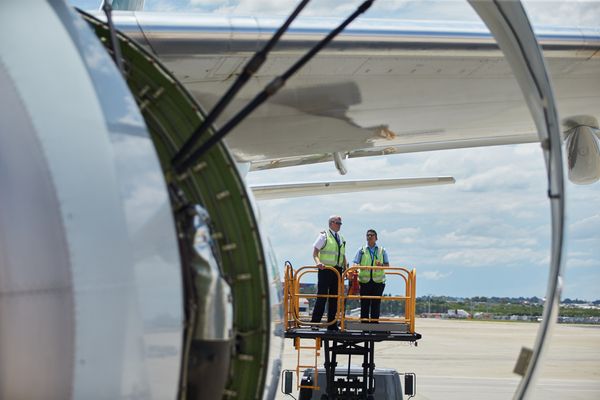 Two ground crew members are standing on a platform near the wing of an aircraft, engaged in a discussion.