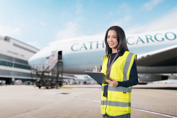 Person in yellow high-visibility vest with clipboard and pen in front of Cathay Cargo airplane.