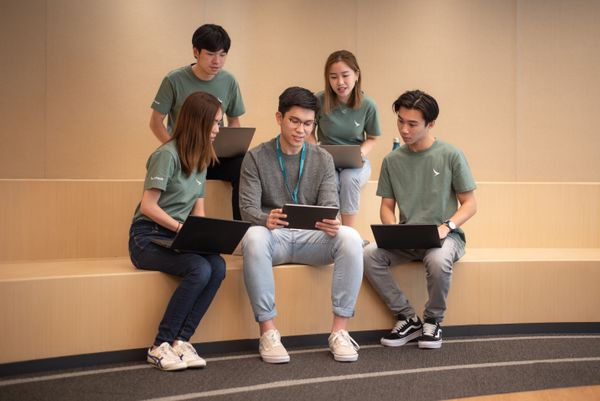 五位同事在灯光温暖、设计现代的办公室中围绕笔记本电脑微笑合作，氛围友好且专业。