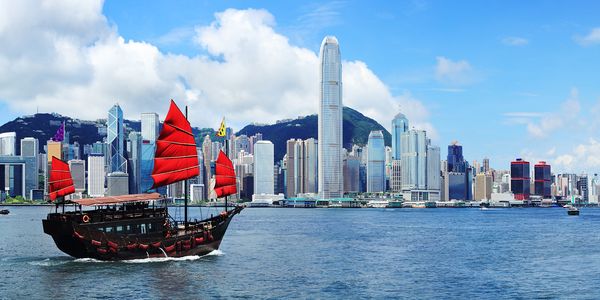 這幅畫面展示了維多利亞港的美麗景色,畫面中有一艘懸掛紅色旗幟的船隻,與後方的城市天際線相映成趣。