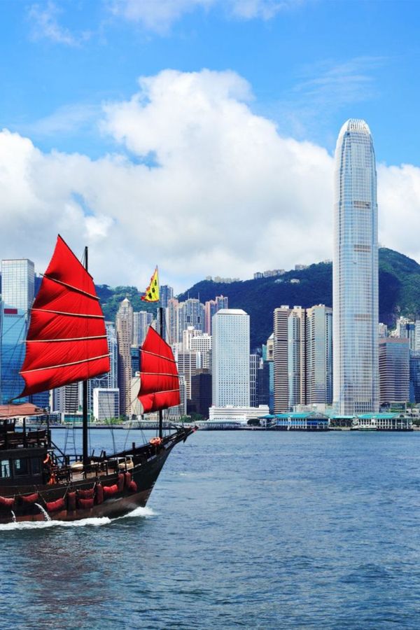 This image showcases a beautiful view of Victoria Harbour, featuring a ship with a red flag in the foreground, complementing the skyline of the city in the background.