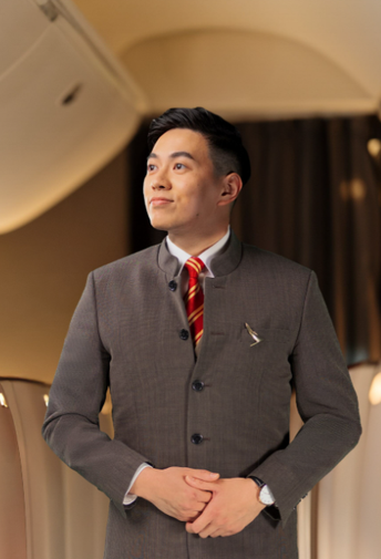A close-up of a male flight attendant in uniform, smiling brightly.