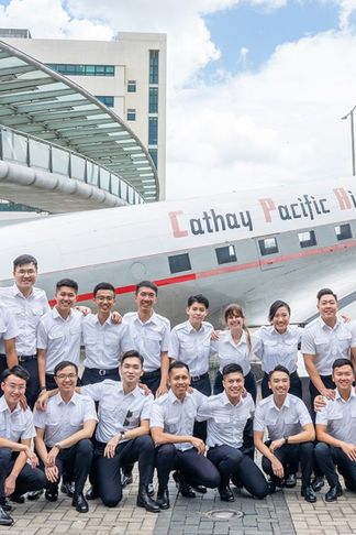 A group of people in uniform poses in front of a Cathay Pacific Airways airplane outdoors on a sunny day.