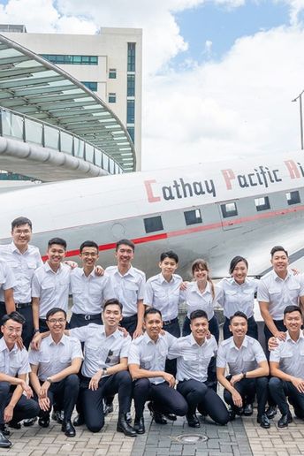 A group of people in uniform poses in front of a Cathay Pacific Airways airplane outdoors on a sunny day