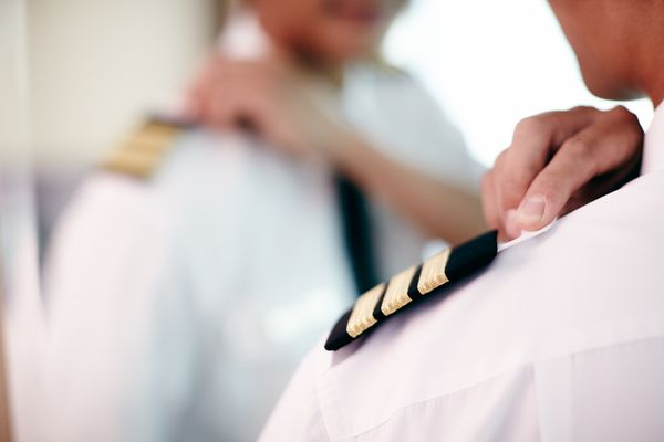 A uniformed first officer faces a mirror, fine-tuning the three gold stripes on his shoulder.