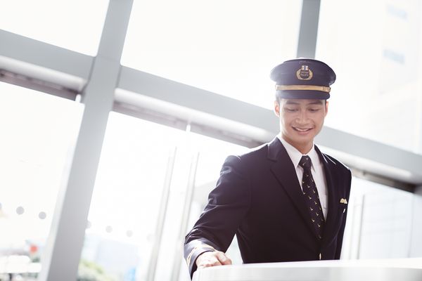 一位穿著飛行員制服、臉部模糊的人站在明亮的機場環境中。