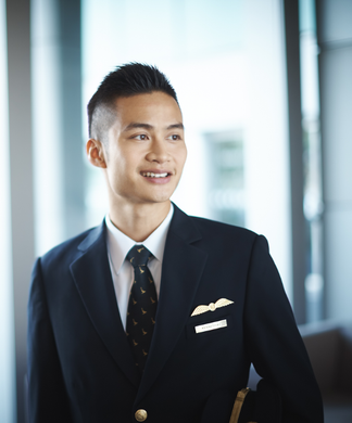 A man in a pilot uniform stands indoors, looking to the side and smiling