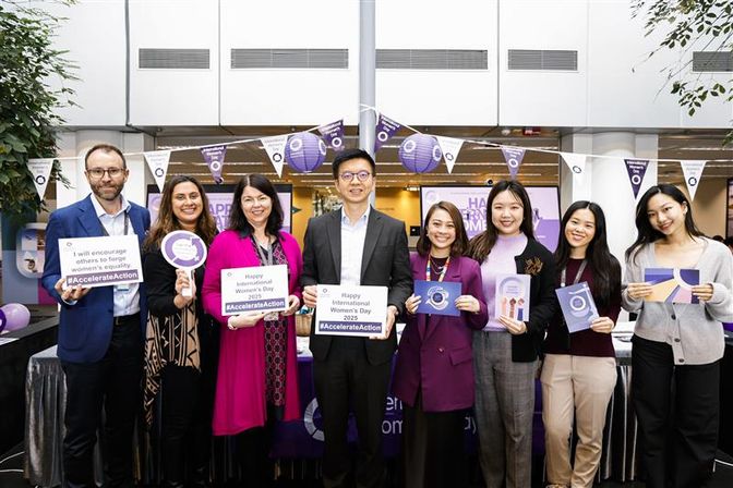 A group of people including CEO Ronald Lam standing in the centre, holding signs celebrating International Women's Day.